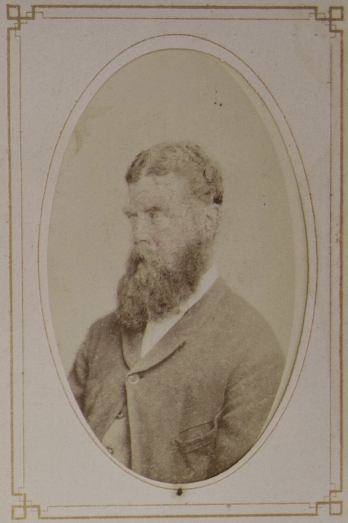 close up of a photo of an older man with a longer bushy beard, short hair, facing on an angle to the side