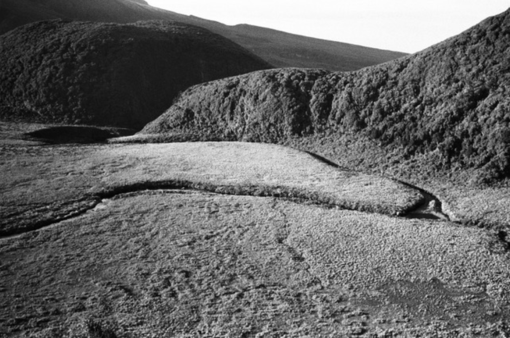 black and white photo of flat swampy foreground with the indentation of a river cutting through it, bracketed by hills